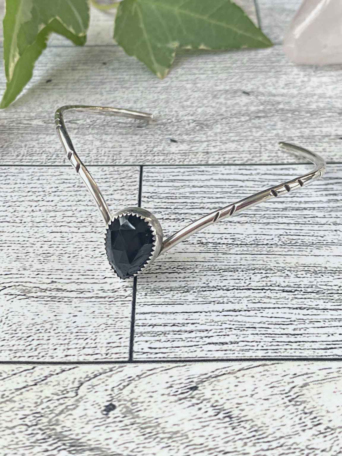 One of a kind handcrafted bracelet.  Handcrafted sterling silver v-shaped bracelet that is set with a pear shaped natural black onyx. Thin and dainty but sturdy bracelet is hand stamped and highlighted.   Ships within 1 to 2 business days. (Not including weekends or holidays)  Black onyx can be used for grounding, protection, and self-control, and as a shield against negative energy. It also enhances discipline, allowing more ease in following through on goals and completing tasks.