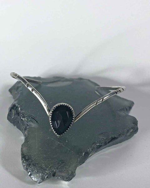 One of a kind handcrafted bracelet.  Handcrafted sterling silver v-shaped bracelet that is set with a pear shaped natural black onyx. Thin and dainty but sturdy bracelet is hand stamped and highlighted.   Ships within 1 to 2 business days. (Not including weekends or holidays)  Black onyx can be used for grounding, protection, and self-control, and as a shield against negative energy. It also enhances discipline, allowing more ease in following through on goals and completing tasks.